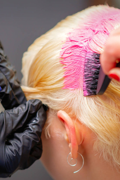 Professionelle Friseurin färbt die Haare der jungen Frau in rosa Farbe. Nahaufnahme des Prozesses der Färbung der Haare rosa - Foto, Bild