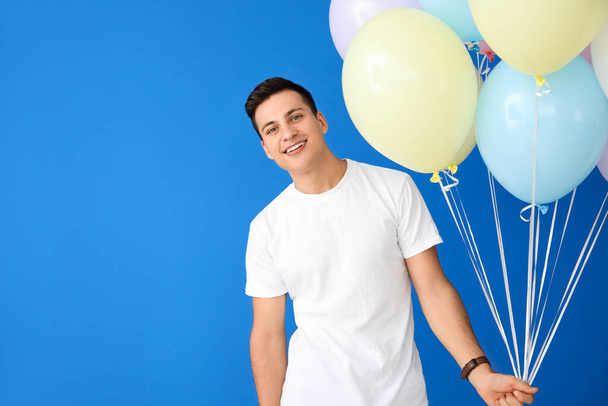 Молодой человек с воздушными шарами на цветном фоне - Фото, изображение