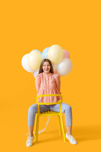 Молодая женщина с воздушными шарами сидит на стуле на фоне цвета - Фото, изображение