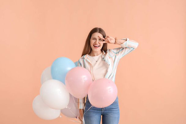 Young woman with balloons showing victory gesture on color background - Fotó, kép