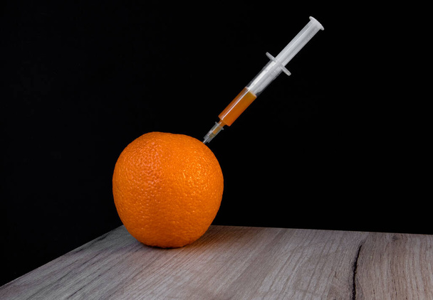 Яркий апельсин на деревянной доске и шприц внутри него извлекает оранжевую жидкость - Фото, изображение