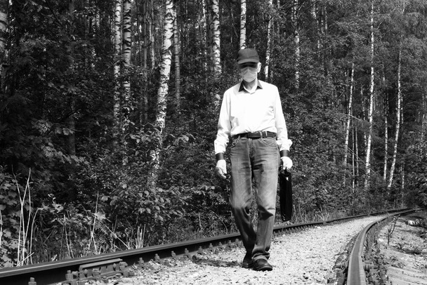 Staruszek w medycznej masce ochronnej i rękawiczkach lateksowych spacerujący po starym torach kolejowych - Zdjęcie, obraz