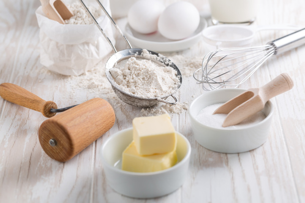 Špaldová mouka, cukr s pečivem a kuchyňské nádobí na bílém dřevěném stole. - Fotografie, Obrázek