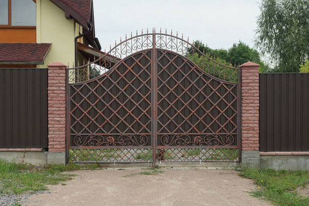 коричневые металлические ворота с выкованным рисунком и частью кирпичного забора на улице - Фото, изображение