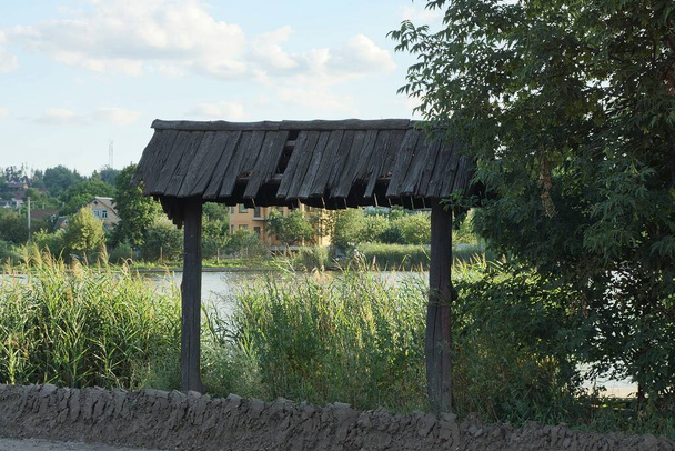 відкриті старі коричневі дерев'яні ворота, вирощені з зеленою рослинністю і травою біля озера
 - Фото, зображення