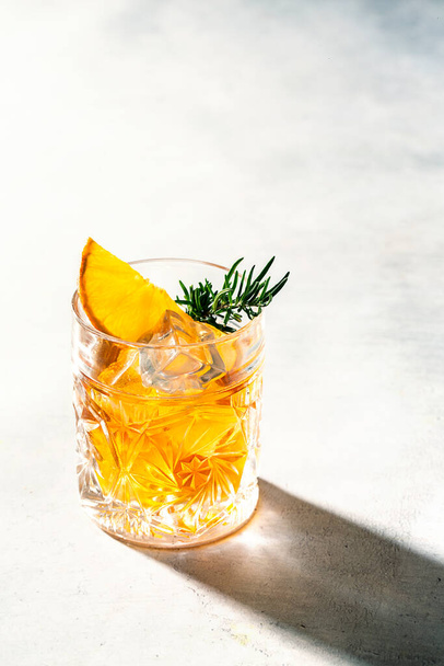 Snijd kristalglas whit oranje vloeistof (whisky) rozemarijn en sinaasappelschijfje. Hard licht - Foto, afbeelding