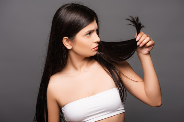 inquiet brunette femme aux cheveux longs regardant pointes fourchues isolé sur noir - Photo, image