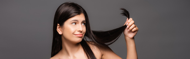 nu sceptique brunette cheveux longs femme regardant split ends isolé sur noir, panoramique shot - Photo, image