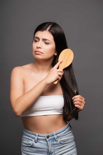 sad brunette woman brushing hair isolated on black - Photo, Image