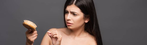 naked worried brunette woman looking at hairbrush isolated on black, panoramic shot - Photo, Image