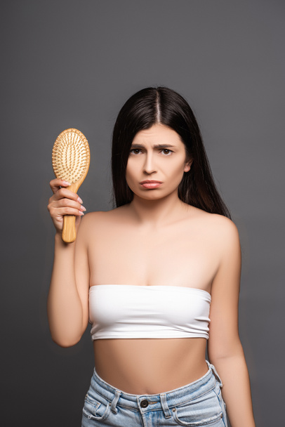 sad brunette woman holding hairbrush isolated on black - Photo, Image