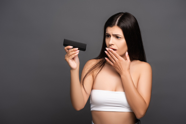 shocked brunette woman looking at comb isolated on black - Photo, Image
