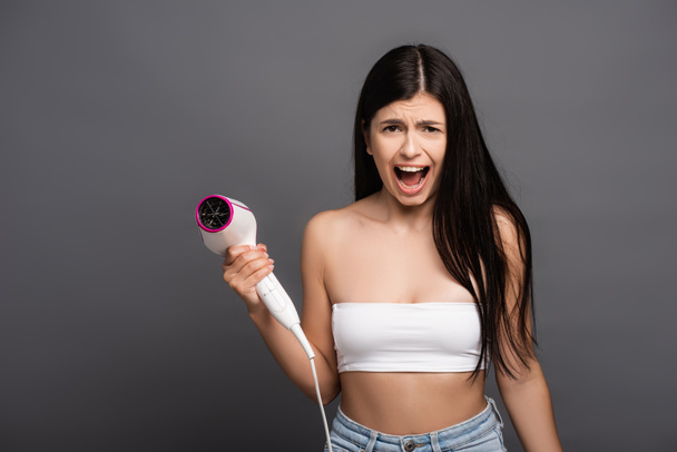 brunette woman holding hair dryer and yelling isolated on black - Photo, Image