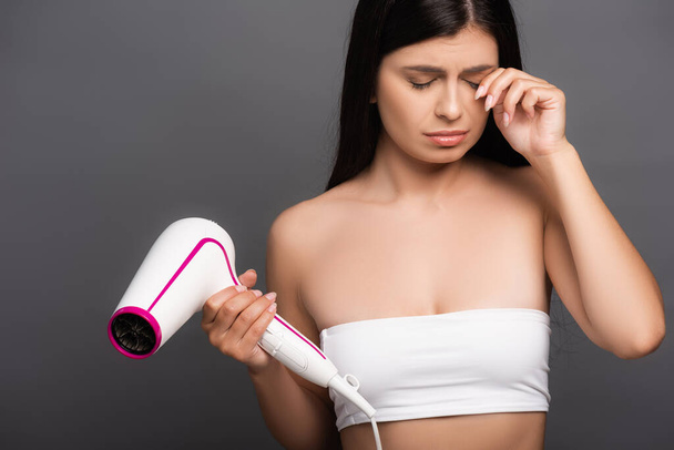 sad brunette woman holding hair dryer and crying isolated on black - Photo, Image