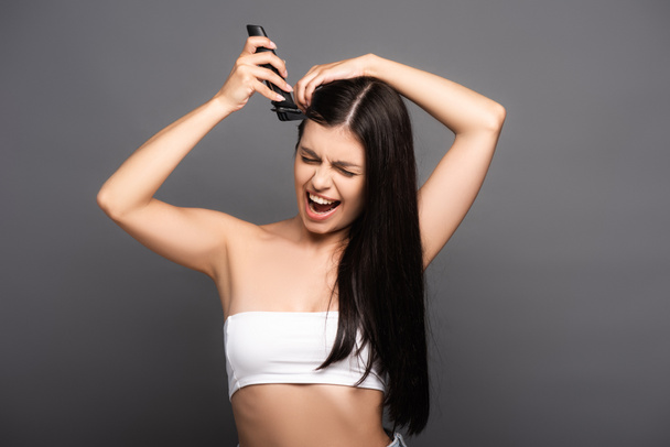 brunette long haired woman shaving head with electric razor and screaming isolated on black - Photo, image
