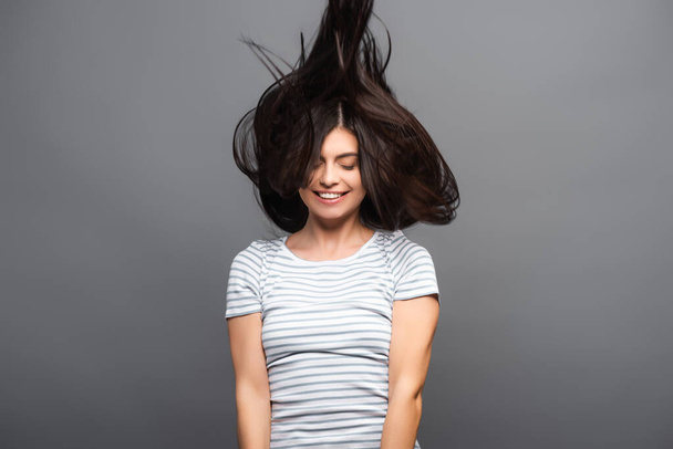 μελαχρινή γυναίκα με μακριά μαλλιά πηδώντας και χαμογελώντας απομονωμένη σε μαύρο - Φωτογραφία, εικόνα