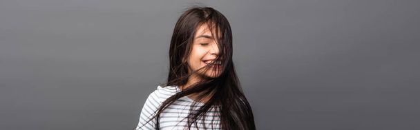 wind blowing through hair of brunette woman with closed eyes isolated on black, panoramic shot - Foto, Imagen