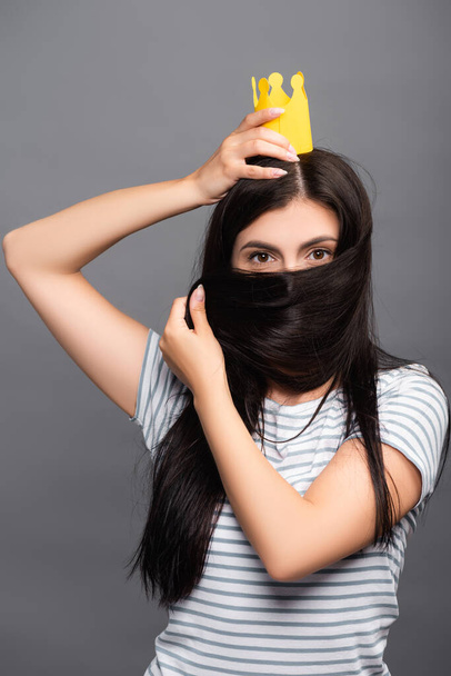 брюнетка жінка в паперовій короні покриває обличчя з волоссям ізольовано на чорному
 - Фото, зображення