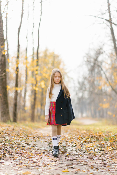 Девушка в школьной красной клетчатой юбке идет по осеннему лесу после школы - Фото, изображение