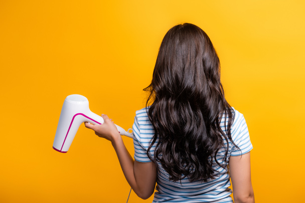 back view of brunette woman with curls holding hairdryer isolated on yellow - Photo, Image