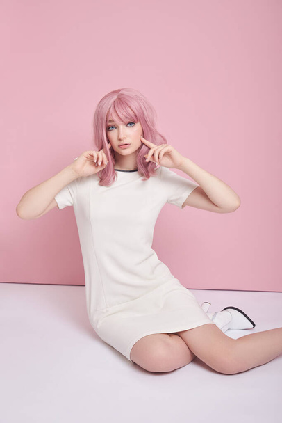 Beautiful girl with long pink hair sitting on the floor, hair coloring. Cute woman on a pink background in a short white dress. Colored hair, perfect hairstyle - Φωτογραφία, εικόνα