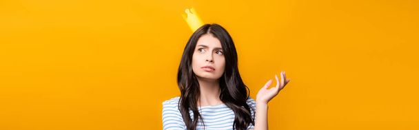 pensive brunette woman in paper crown looking away isolated on yellow, panoramic shot - Foto, immagini