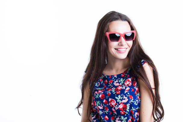 Smiling attractive woman in dress and sunglasses posing on white wall. - 写真・画像