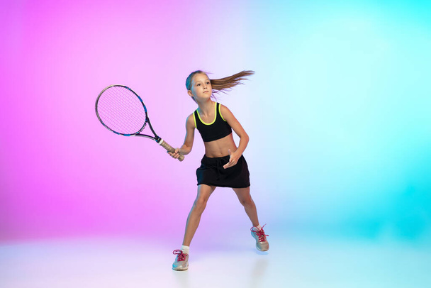 Little tennis girl in black sportwear isolated on gradient background in neon light - Foto, imagen