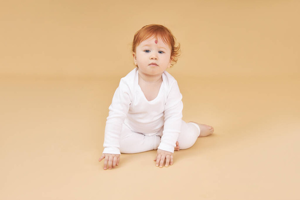 Little red-haired baby girl is playing on a beige background. Big mole on the forehead, not like everyone else - Foto, Imagem