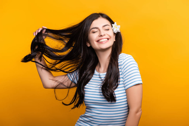 brunette young woman with flowers in hair and closed eyes smiling isolated on yellow - Foto, afbeelding