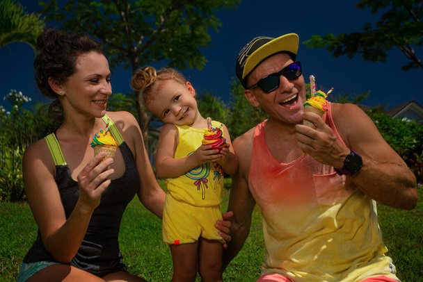 Молодая счастливая семья проводит выходные в парке. Они едят мороженое.. - Фото, изображение