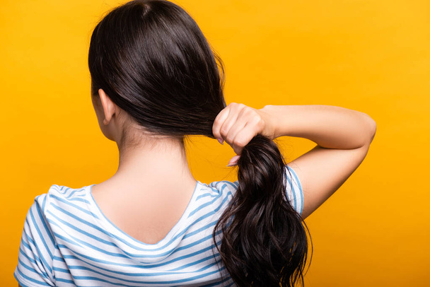 zpět pohled na bruneta žena s kudrlinkami drží vlasy izolované na žluté - Fotografie, Obrázek