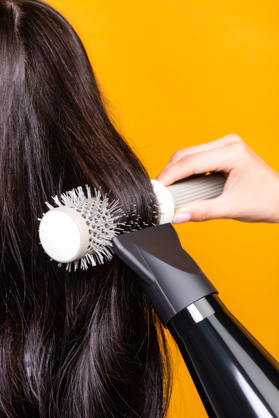 cropped view of hairdresser using hairdryer and brush isolated on yellow - Foto, Imagen