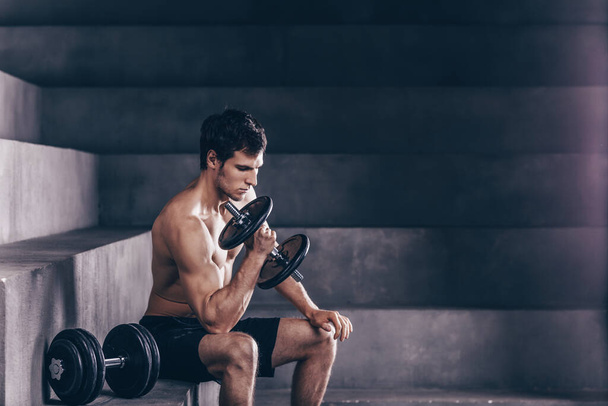 Muscular bodybuilder guy doing exercises with dumbbells on dark background. - Fotoğraf, Görsel
