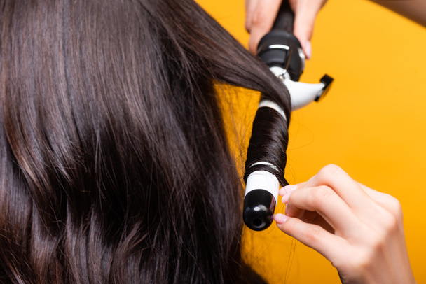 cropped view of hairdresser using curling iron isolated on yellow - Valokuva, kuva