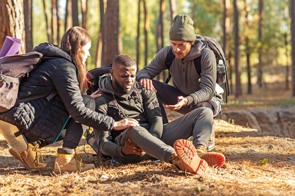 Friends helping african injured guy while hiking by forest - Foto, Bild
