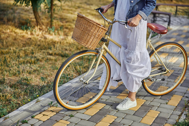 Mujer elegante sosteniendo el manillar de una bicicleta de ciudad con cesta - Foto, Imagen