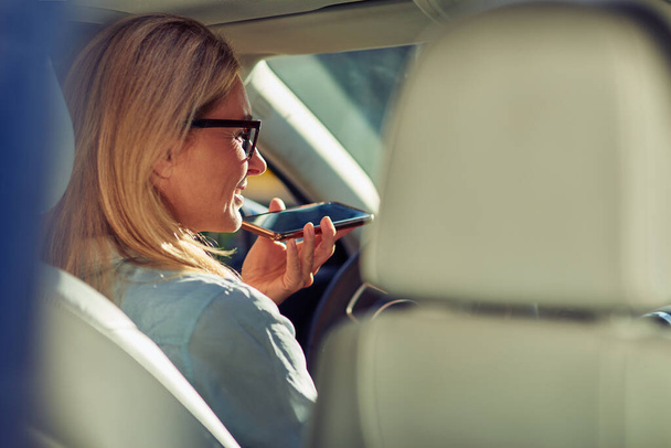 Business talk. Rear view of a beautiful middle aged woman sitting behind steering wheel in a car, talking on phone and smiling - Foto, imagen