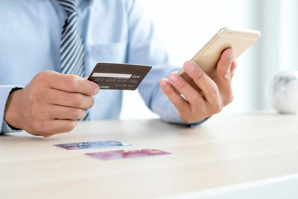 A mão do empresário está segurando um cartão de crédito e usando um smartphone para compras on-line e pagamento pela internet no escritório. - Foto, Imagem
