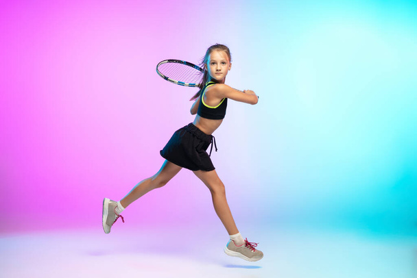 Little tennis girl in black sportwear isolated on gradient background in neon light - Photo, Image