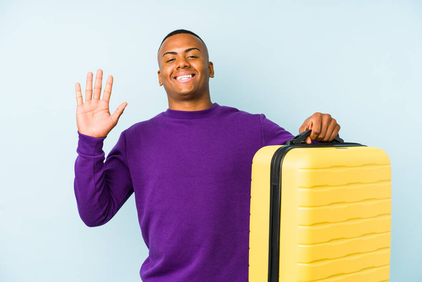młody podróżnik człowiek trzymając walizkę samotny uśmiech wesoły pokazując numer pięć z palcami. - Zdjęcie, obraz