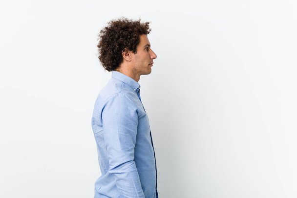 Jonge krullende volwassen man draagt een elegante shirt staren naar links, zijwaarts poseren. - Foto, afbeelding