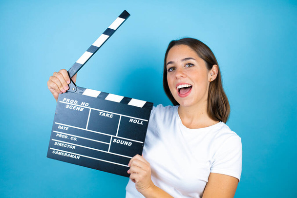 Young beautiful woman over isolated blue background holding clapperboard very happy having fun - Photo, Image