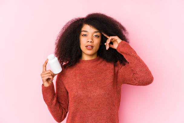 Young afro woman holding a vitamins isolated Young afro woman holding a vitaminspointing temple with finger, thinking, focused on a task. - Foto, afbeelding