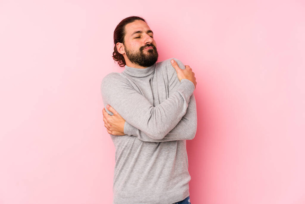 Young long hair man isolated on a pink background hugs, smiling carefree and happy. - Photo, image