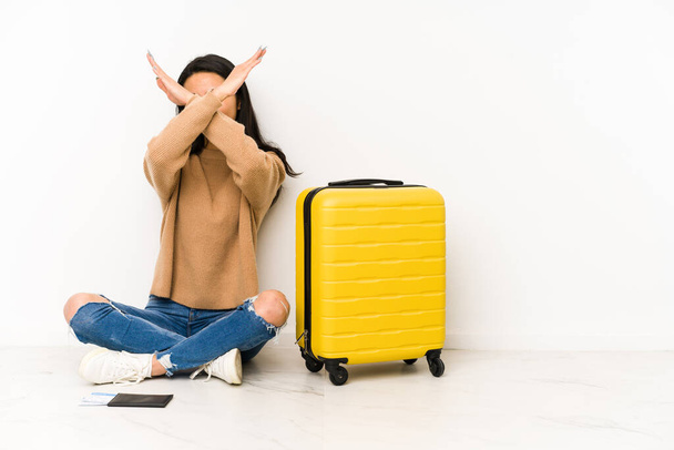 Giovane donna viaggiatrice cinese seduta sul pavimento con una valigia isolata tenendo due braccia incrociate, concetto di negazione. - Foto, immagini