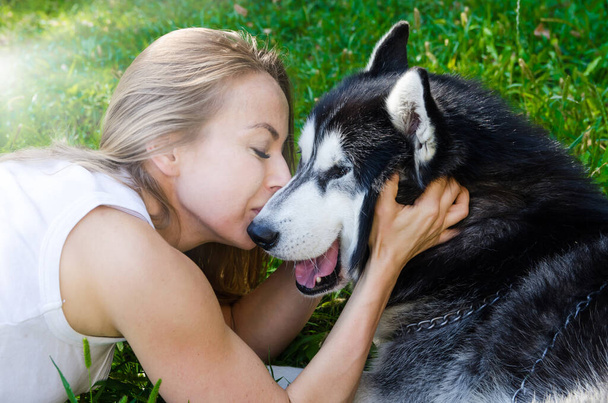 young beautiful girl kisses a dog on a background of green grass. Close-up. - Photo, Image