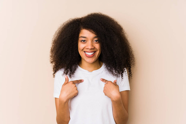 Joven mujer afroamericana sorprendida señalando con el dedo, sonriendo ampliamente. - Foto, imagen