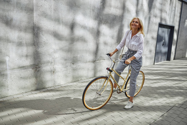 Şık giyinmiş, mutlu, beyaz bir kadın bisiklete binmeye başlıyor. - Fotoğraf, Görsel