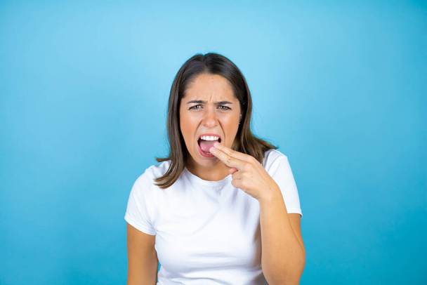 Young beautiful woman over isolated blue background disgusted with her hand inside her mouth - Photo, Image